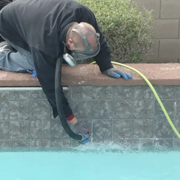 Technician cleaning a pool wall with a hose